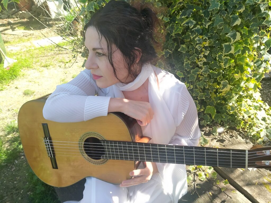 L'immagine mostra la musicista Veronica Barsotti seduta che scruta la natura che la circonda appoggiata con il braccio destro sulla chitarra realizzata dal Liutaio Roberto de Miranda
